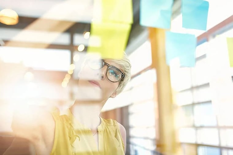 Two creative millenial small business owners working on social media strategy brainstorming using adhesive notes in windows